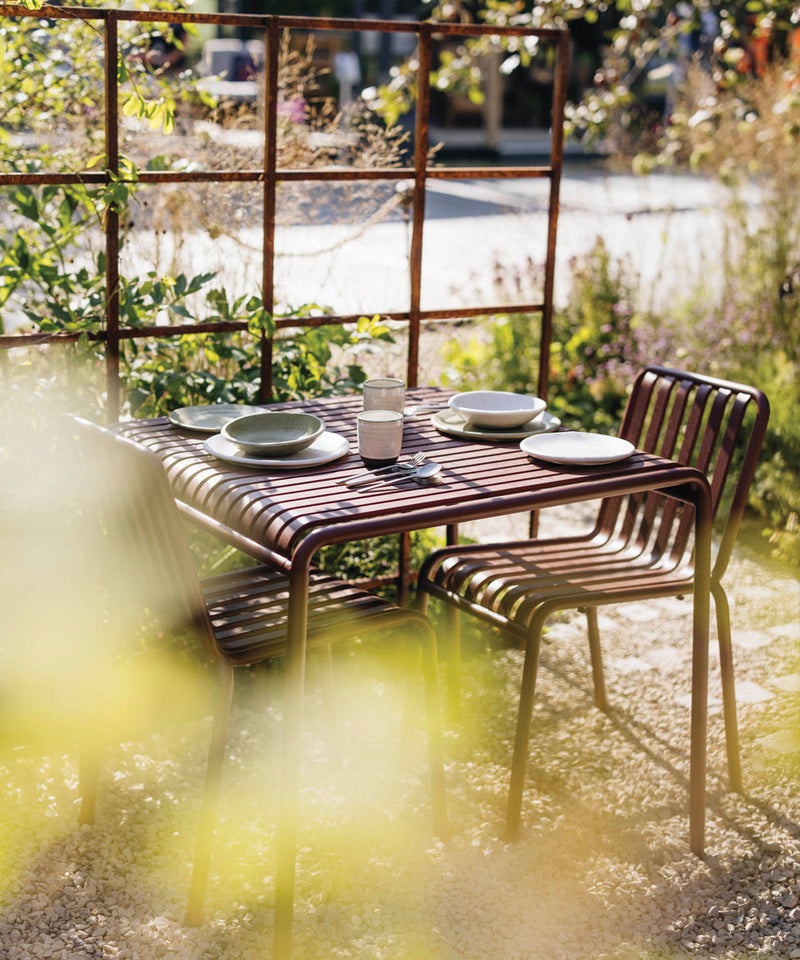 HAY Palissade table setting in Iron Red framed by green vine leaves and wooden accents in the RHS Badminton garden.