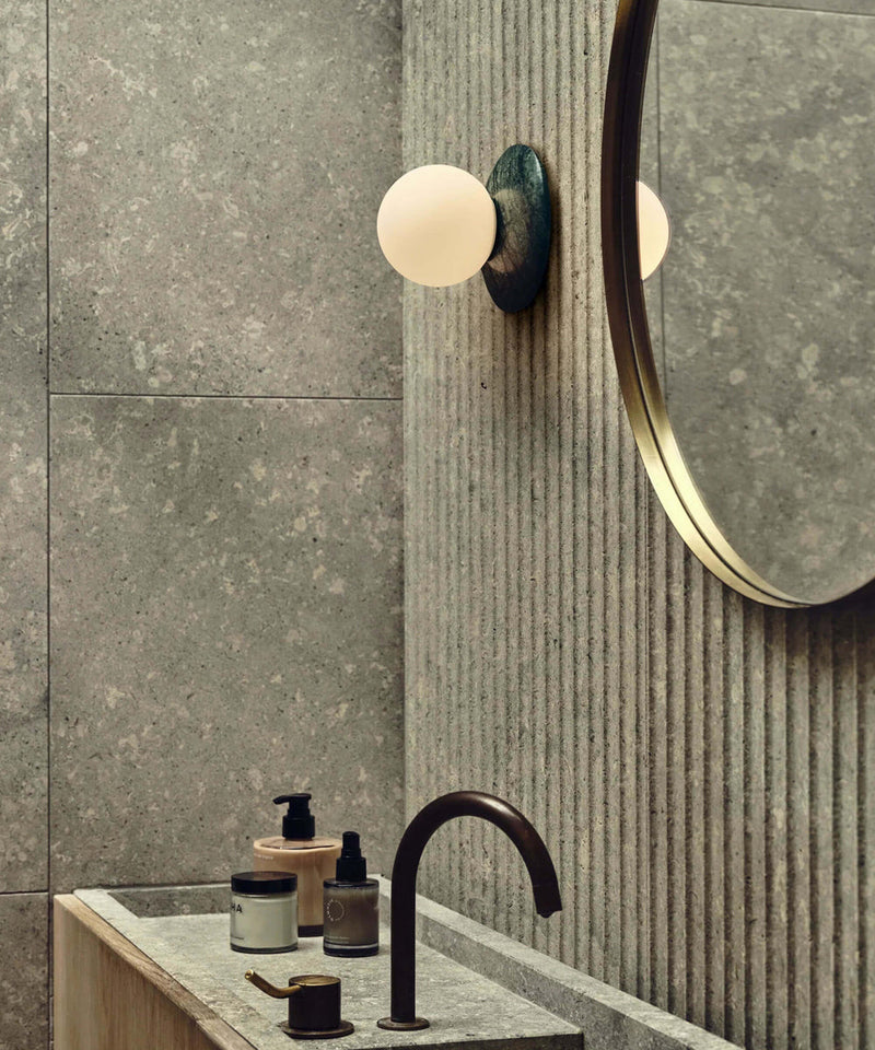 A bathroom featuring natural materials and the J.Adams Orbit Stone wall light next to the mirror over a stone sink