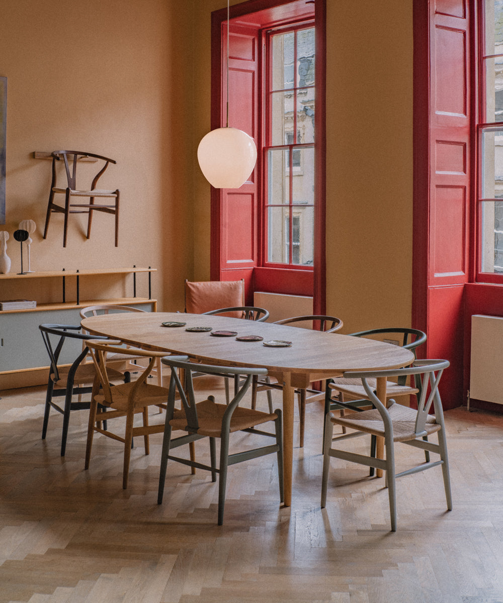 A collection of CH24 Wishbone chairs in a range of colours and wood finishes all around a large oval dining table