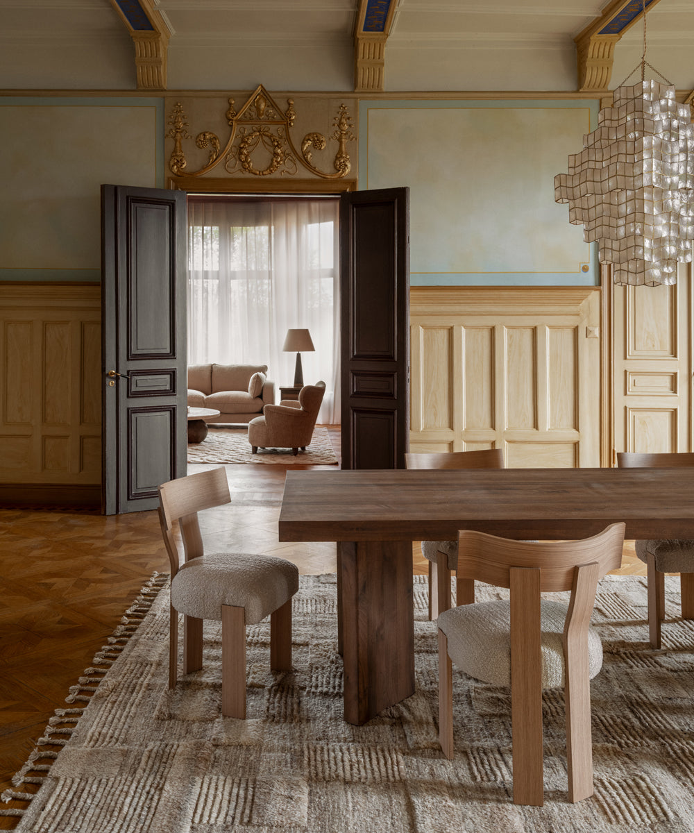 A grand dining room with a dark wooden table and a range of dining chairs with a sheepskin upholstered seat all sat on a woven cream rug