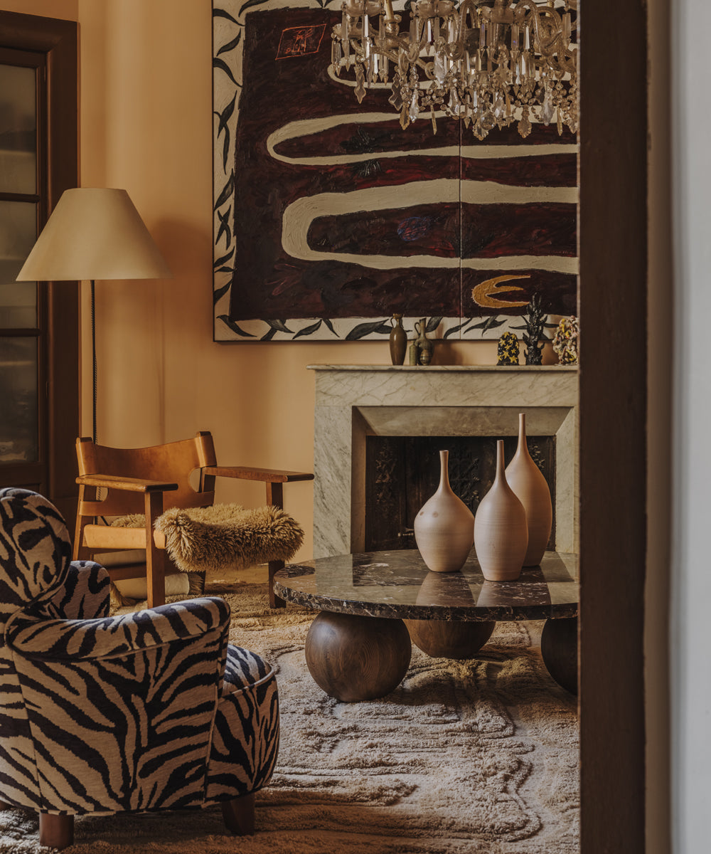 In another lounge area, a dramatic antique chandelier hangs low over the space, centring the room naturally. Underneath sits the Dusty Deco Sphere Sofa Table