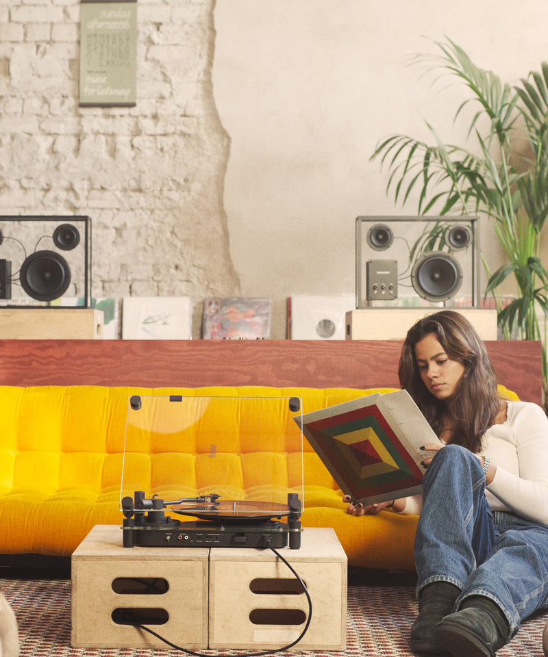 A living which shows a record player and two transparent speakers
