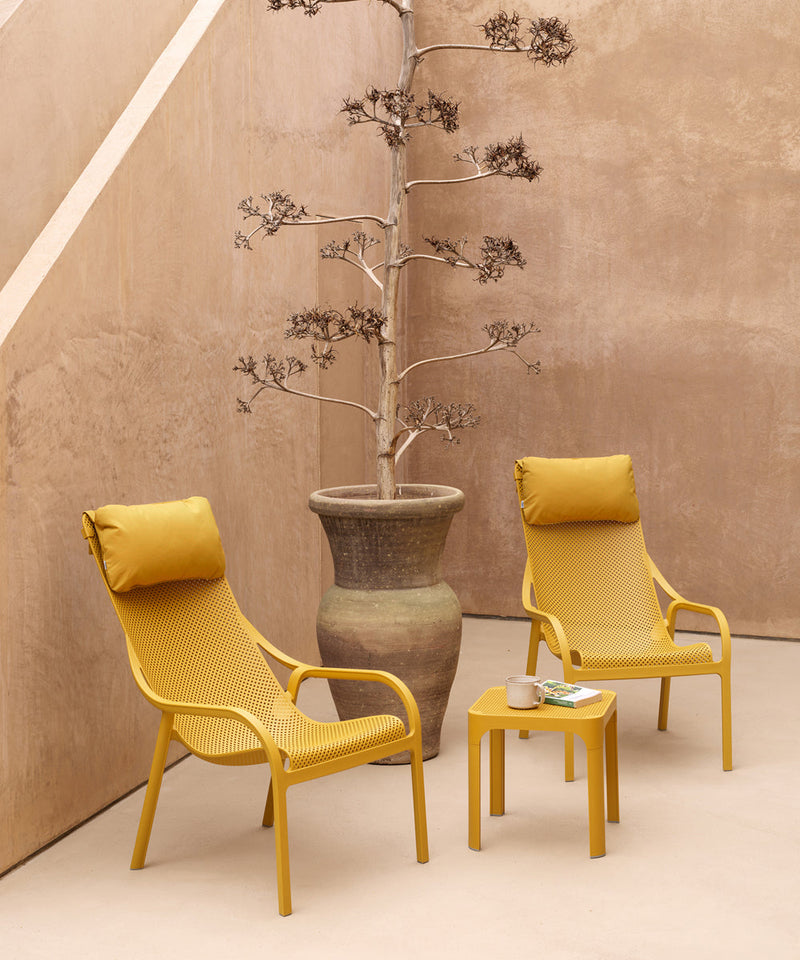 A set of two Nardi Lounge Chairs and a small table  finished in a bright yellow in a small courtyard.