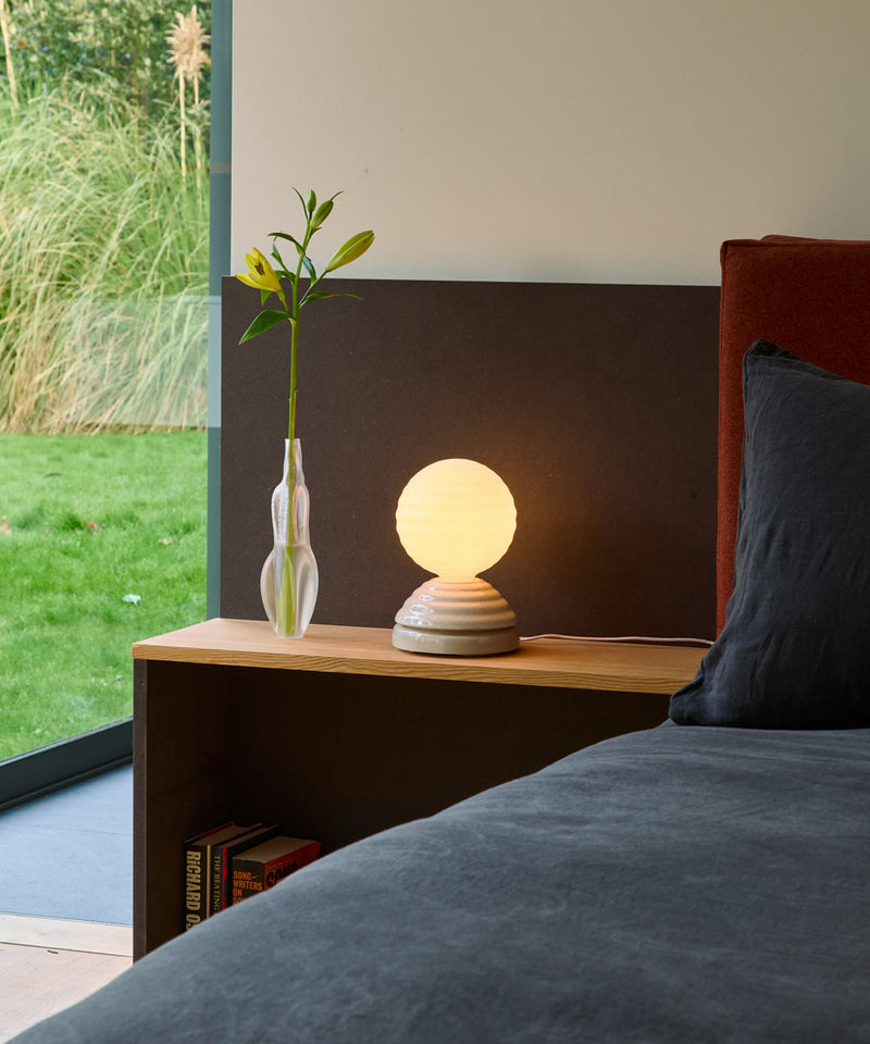 The Tala WAKE bedside lamp on a wooden table next to a flower