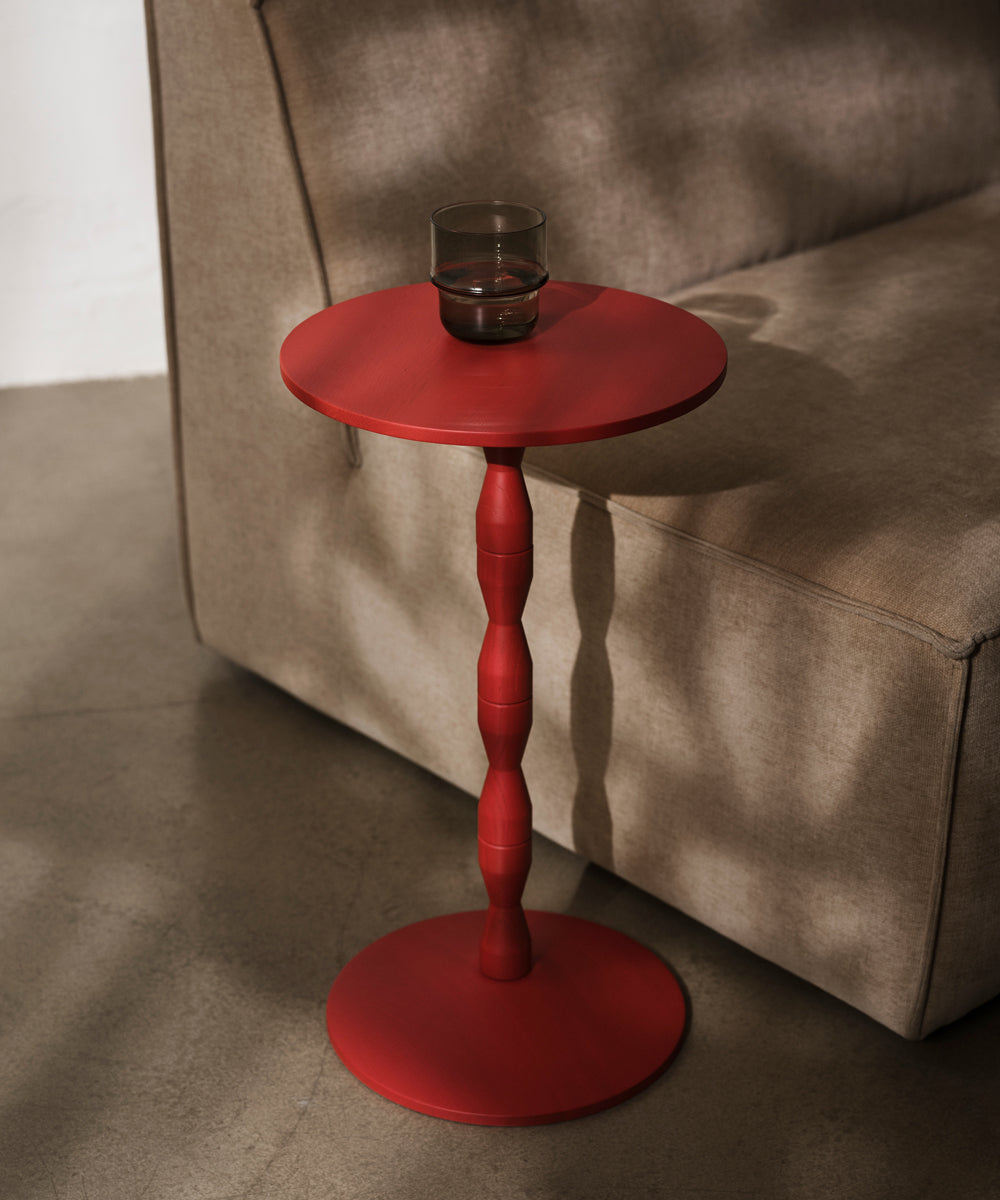 A red side table with a glass on next to a sofa