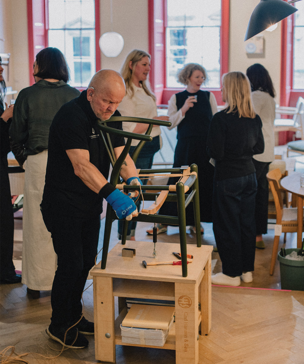 Craftsman hand-weaving a Wishbone Chair in a showroom setting